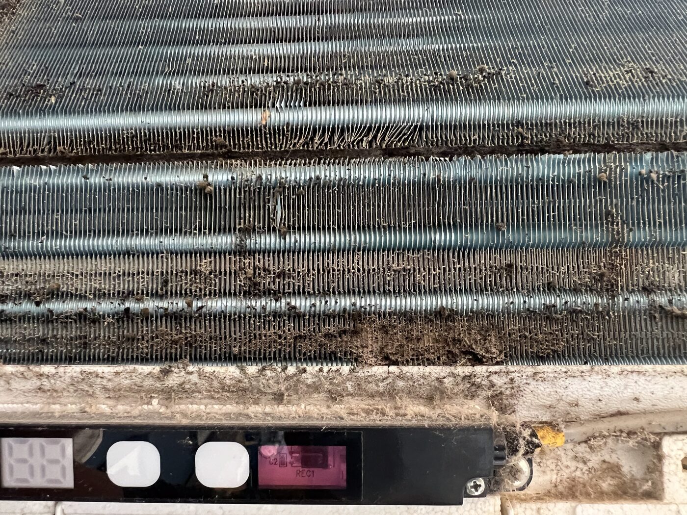 Close-up of heavily contaminated AC evaporator coils with thick dust and biological fouling between the fins.